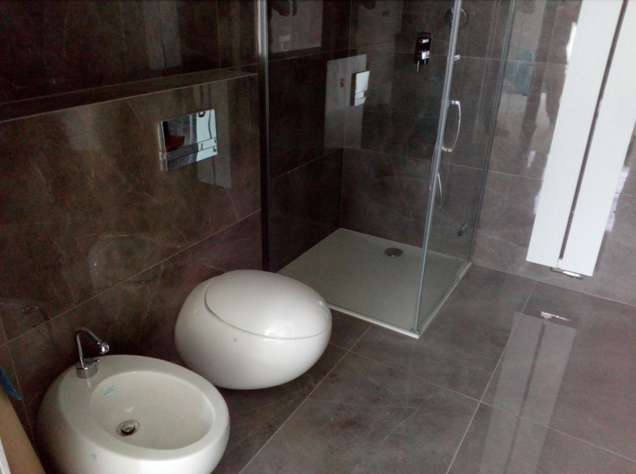 Nowoczesna łazienka z brązowymi płytkami: kabina prysznicowa z odpływem liniowym, okrągła umywalka z baterią i kulisty bidet.