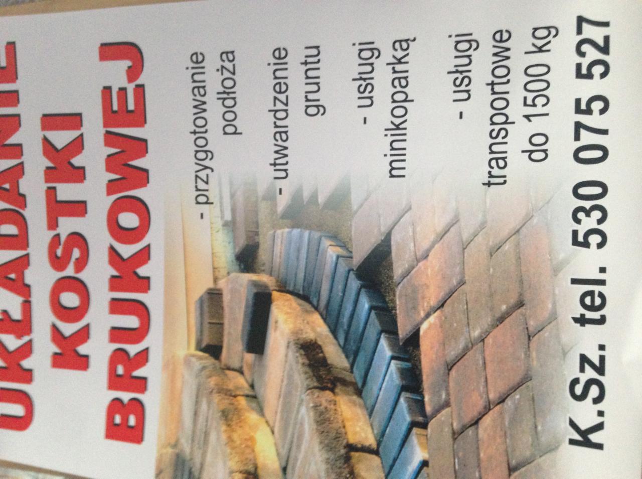 Ujęcie z bliska ulotki reklamowej firmy brukarskiej z informacją o układaniu kostki, przygotowaniu podłoża, utwardzaniu gruntu, usługach minikoparką i transporcie do 1500 kg, widoczne ułożone...