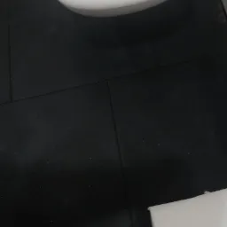 Częściowy widok czarnej, matowej podłogi z płytek w łazience, z fragmentem białej muszli klozetowej i białym elementem wyposażenia w rogu kadru.