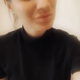 Portret kobiety z delikatnym makijażem, ubranej w czarną bluzkę z golfem, spoglądającej w obiektyw z lekkim uśmiechem.