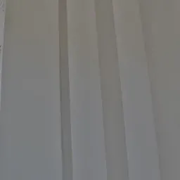 Gładka, szara ściana z dekoracyjnymi, pionowymi wgłębieniami, oświetlona z góry, z fragmentem siatki zbrojeniowej widocznym w lewym górnym rogu.