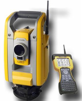 Żółto-szary tachimetr Trimble z anteną i kontrolerem w kolorze żółtym na jasnym tle.