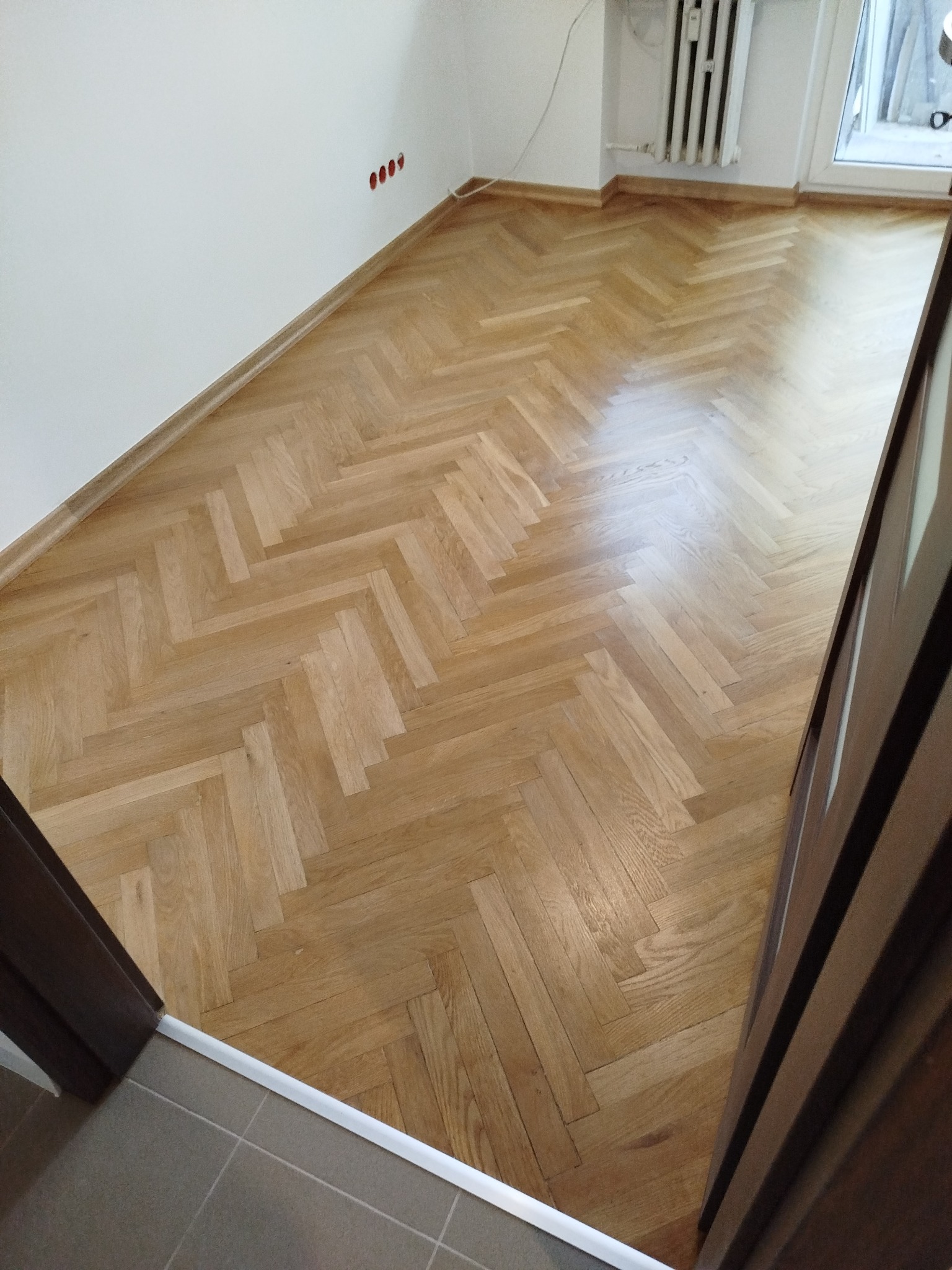 Jasny parkiet ułożony we wzór jodełki w odnowionym pokoju, widok z progu drzwiowego.