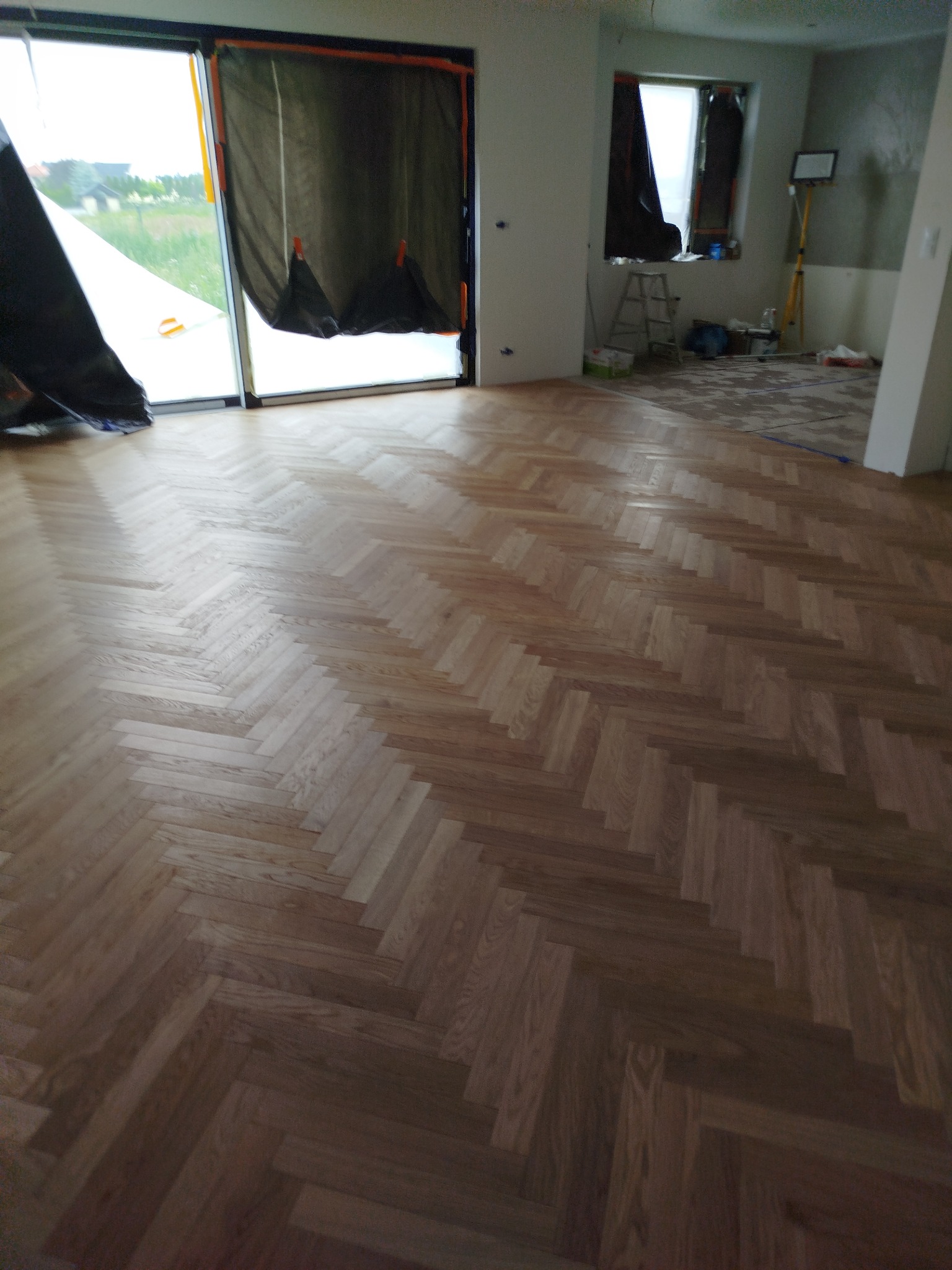 Ułożony parkiet w jodełkę, widok z góry, z zabezpieczonymi oknami folią malarską. Prace parkieciarskie w Niedrzwicy Dużej.
