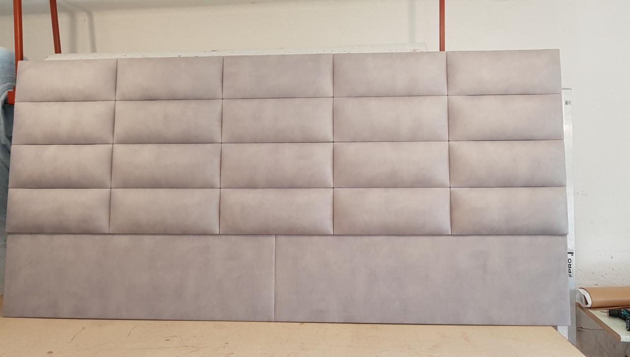 Tapicerowany zagłówek do łóżka w odcieniach beżu, składający się z prostokątnych paneli z widocznymi przeszyciami, ułożonych w regularny wzór.