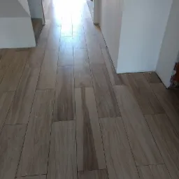 Ułożona podłoga z płytek imitujących drewno w jasnym odcieniu, widok z perspektywy wejścia do pomieszczenia, ściany w trakcie wykańczania.