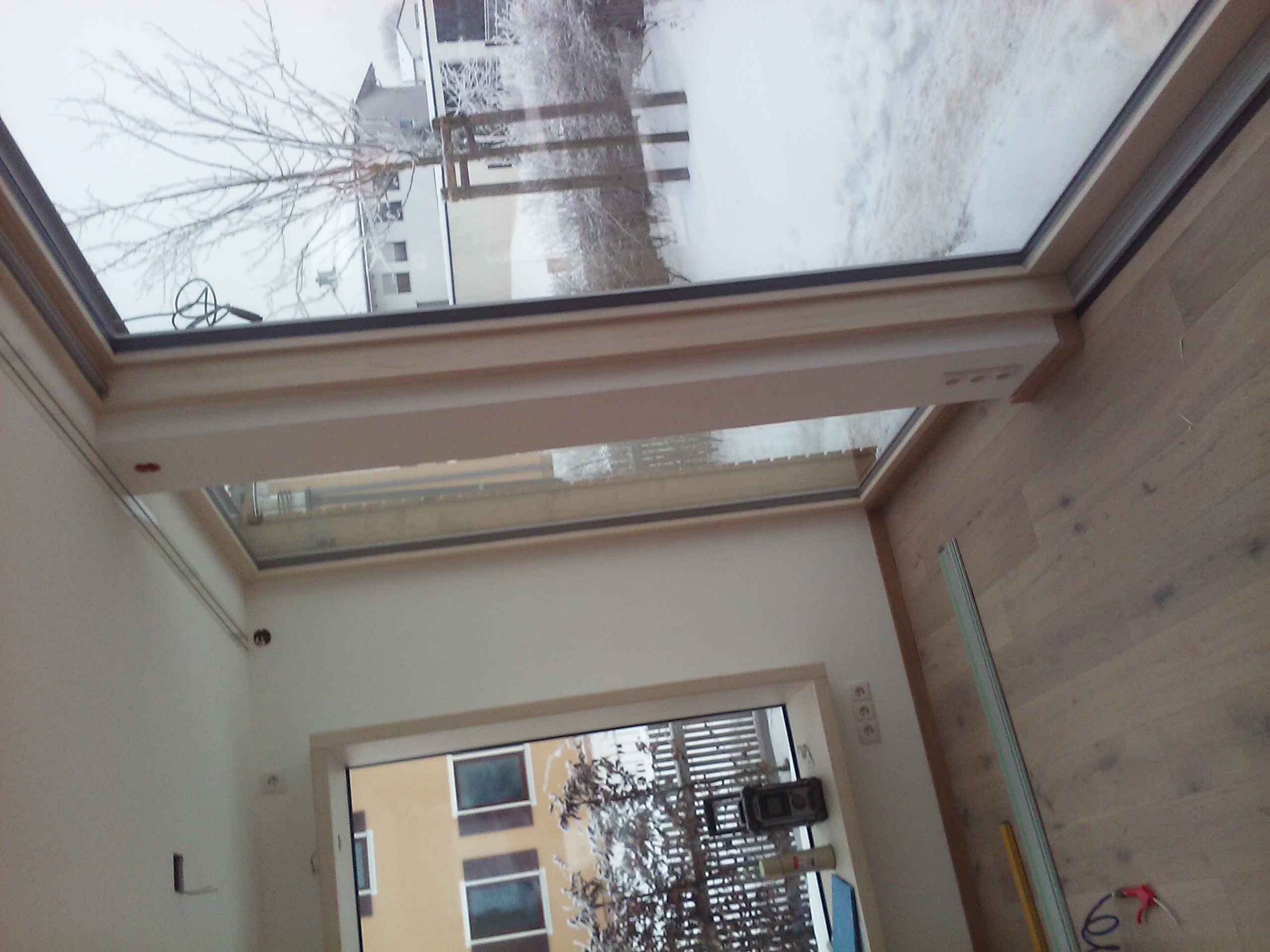 Widok z wnętrza na zamontowane okno dachowe w Lublińcu, za oknem zimowy krajobraz z ośnieżonymi drzewami i budynkami.