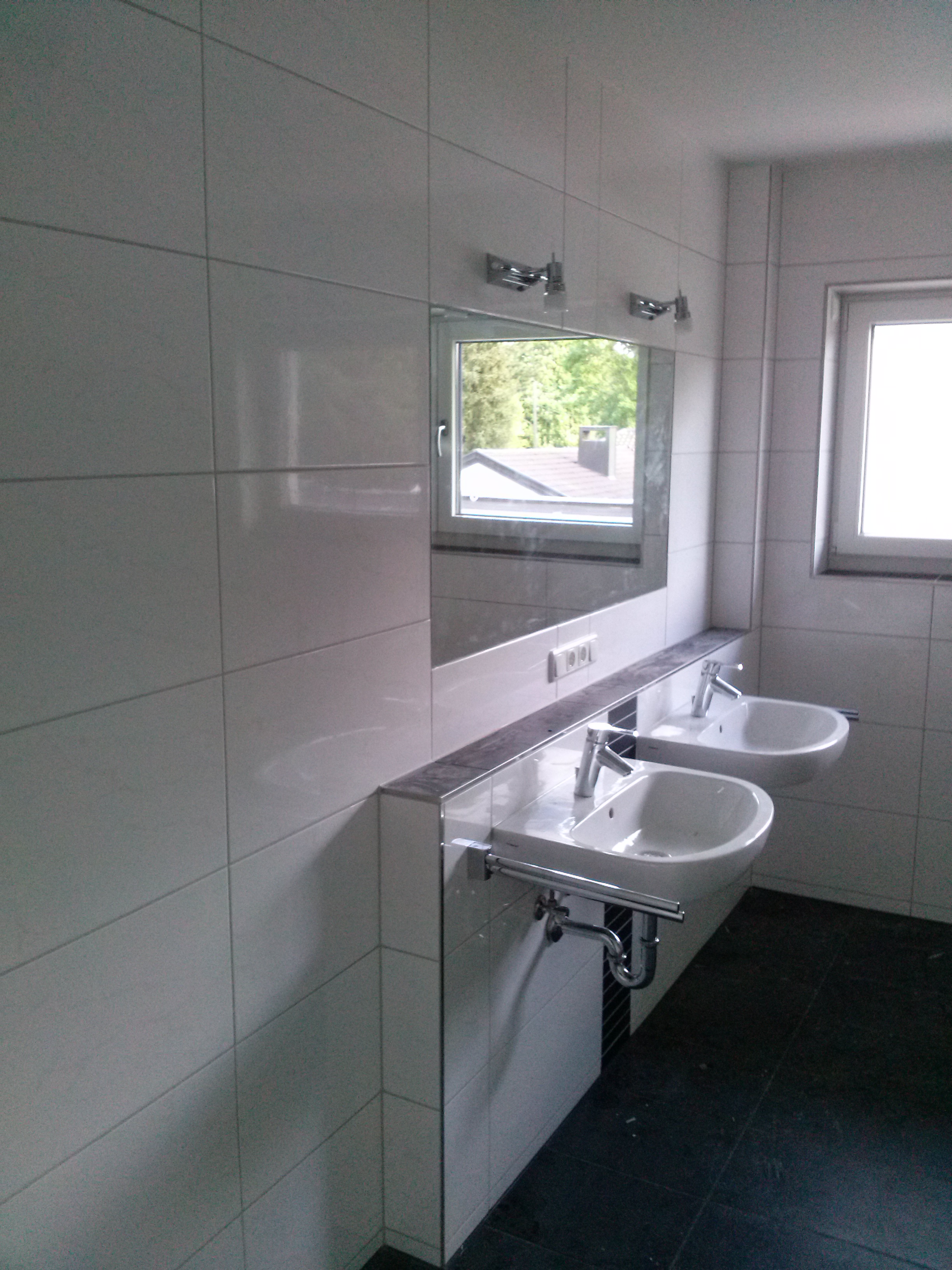 Jasna łazienka z dwoma umywalkami nablatowymi, chromowanymi bateriami i lustrem, w którym odbija się okno z widokiem na zieleń.