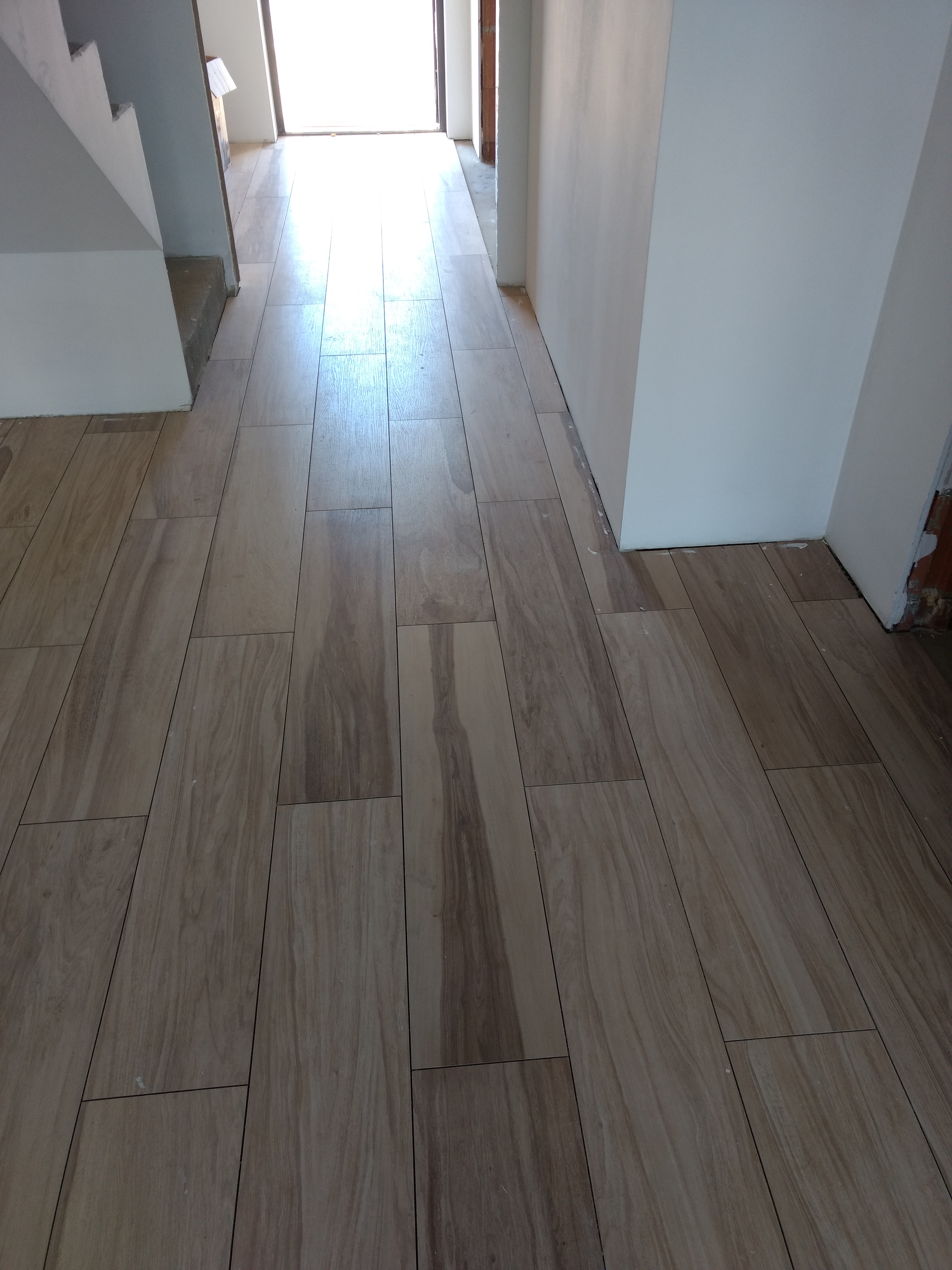 Ułożona podłoga z płytek imitujących drewno w jasnym odcieniu, widok z perspektywy wejścia do pomieszczenia, ściany w trakcie wykańczania.