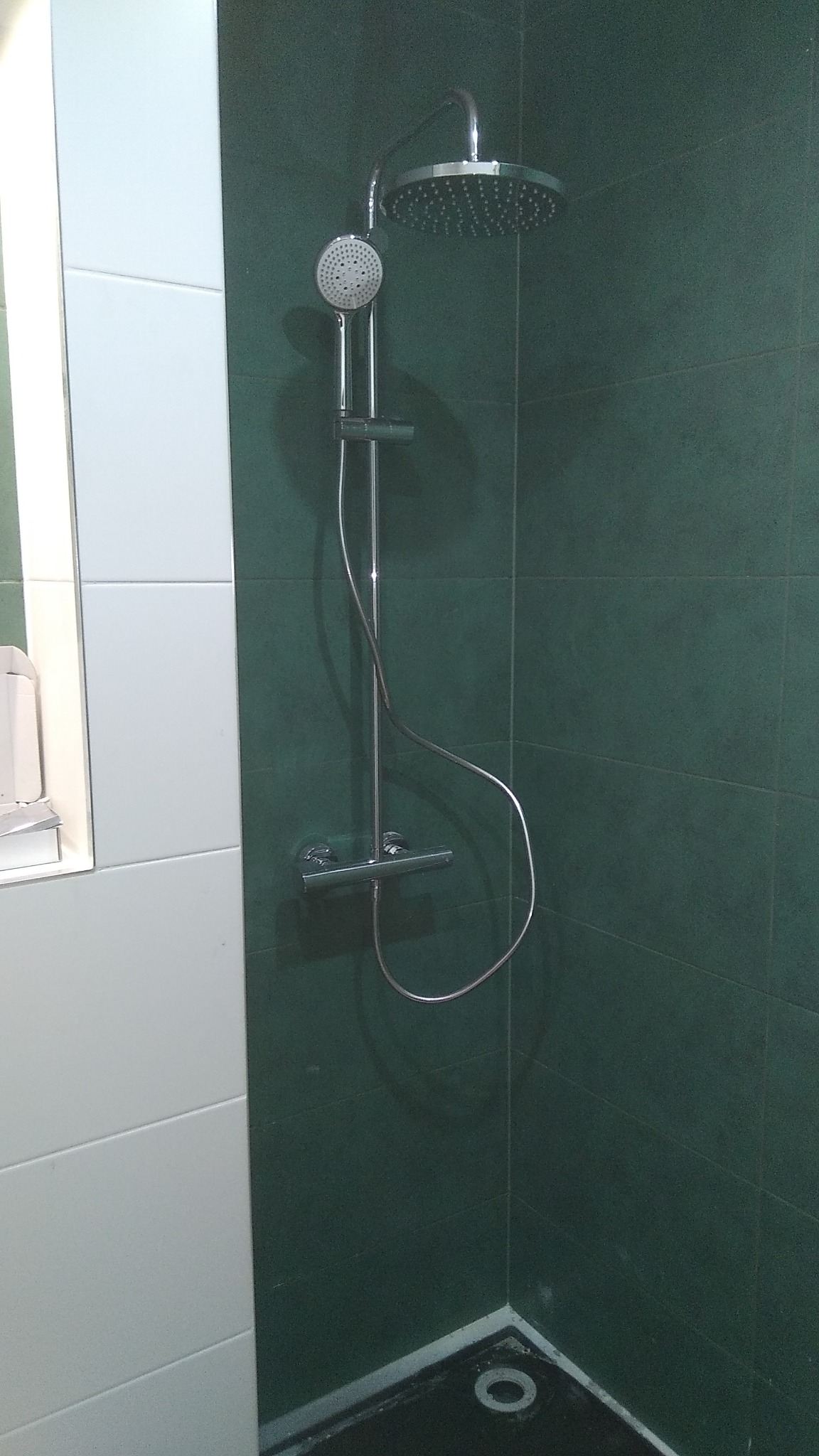 Nowoczesna kabina prysznicowa z deszczownicą i baterią termostatyczną na tle zielonych i białych płytek w łazience.