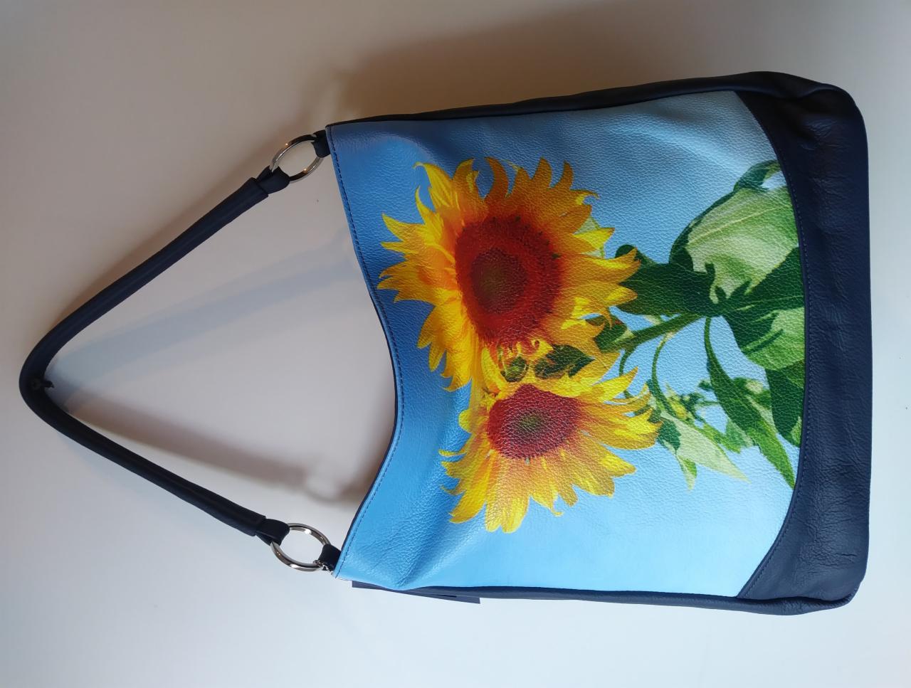 Niebieska torebka z motywem słoneczników, granatowe wykończenia i uchwyt, srebrne kółka mocujące uchwyt.
