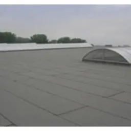 Płaski dach pokryty papą termozgrzewalną w szarym kolorze, widoczne świetliki kopułowe, pochmurne niebo w tle.