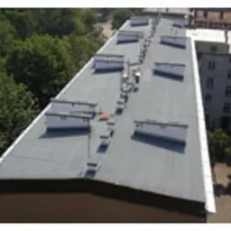 Płaski dach budynku pokryty papą termozgrzewalną, widoczne kominy wentylacyjne, ujęcie z góry.