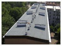 Płaski dach budynku pokryty papą termozgrzewalną, widoczne kominy wentylacyjne, ujęcie z góry.