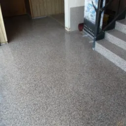 Szara posadzka żywiczna typu Graniflex z widocznymi schodami pokrytymi tym samym materiałem i fragmentem okna po lewej stronie.