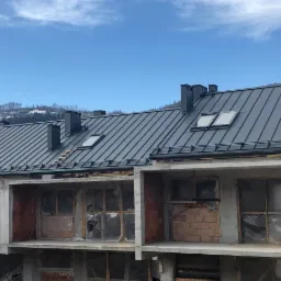 Nowy, grafitowy dach z blachy na budynku w stanie surowym otwartym, z widocznymi oknami dachowymi i kominami, na tle górskiego krajobrazu.