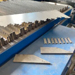 Blacha z wyciętymi elementami leżąca na niebieskim stole roboczym obok maszyny do cięcia; widoczne detale i gotowe elementy.