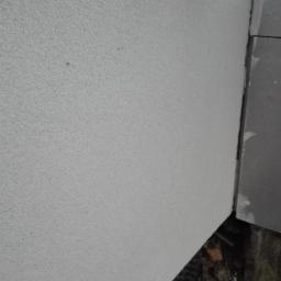 Kontrast - Szara ściana z nierówną fakturą, stykająca się z szarym elementem konstrukcyjnym przy podłożu z gruzem.