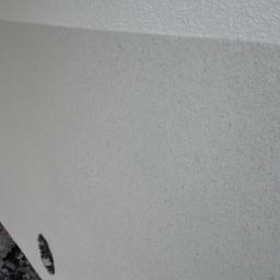 Kontrast - Ściana z nałożoną szarą strukturą, widoczny fragment instalacji i gruz na podłodze.