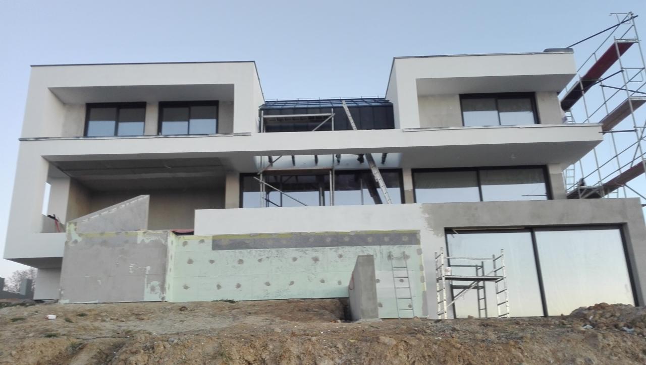 Nowoczesny dom w trakcie wykończenia elewacji zewnętrznej, widoczne rusztowania, ocieplenie styropianem i częściowo nałożona warstwa szpachli.