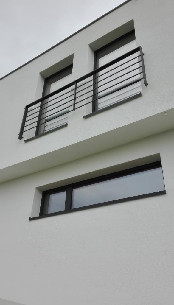 Elewacja budynku z białym tynkiem strukturalnym, czarne ramy okienne i balkon z metalową balustradą.