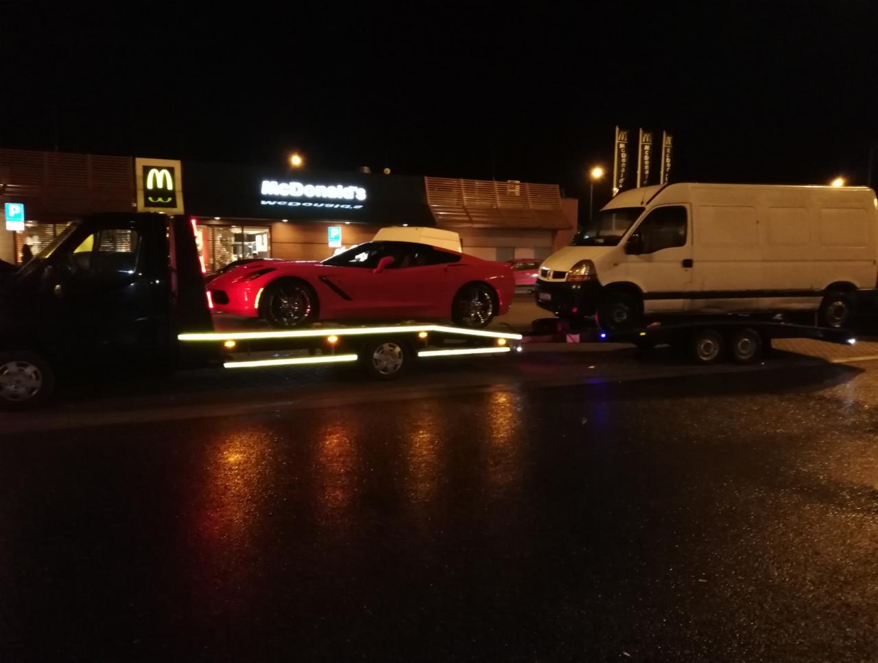 Laweta z czerwonym sportowym samochodem Corvette na lawecie, obok biały bus na lawecie, nocne ujęcie na tle restauracji McDonald's w Smólsku Dużym.