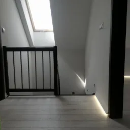 Jasne poddasze z drewnianą barierką, widoczne panele podłogowe i okno dachowe w skosie, oświetlenie LED wzdłuż ściany.