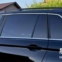 Ciemne szyby w czarnym samochodzie typu kombi, widoczny napis z nazwą firmy i numerem telefonu na karoserii.