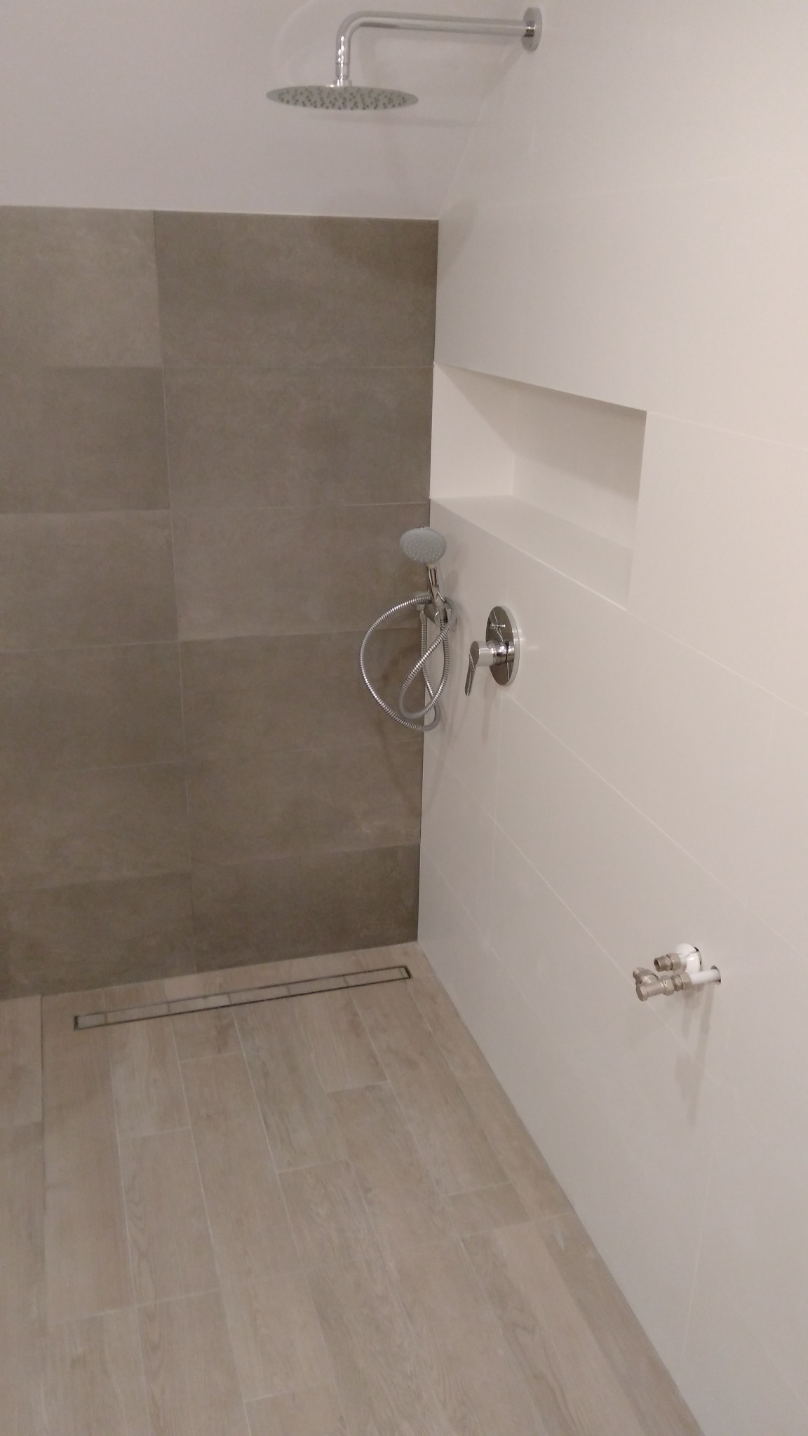 Nowoczesna kabina prysznicowa z deszczownicą, odpływem liniowym i półką w ścianie, wykończona płytkami w odcieniach szarości i beżu.