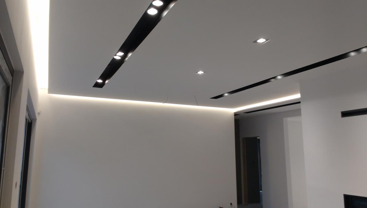 Nowoczesne oświetlenie sufitowe z czarnymi wstawkami i listwami LED w pomieszczeniu w Wolsztynie po remoncie.
