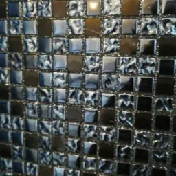 Mozaika ścienna z małych, kwadratowych płytek w odcieniach szarości, srebra i brązu, z efektem lustrzanym i nieregularną fakturą.