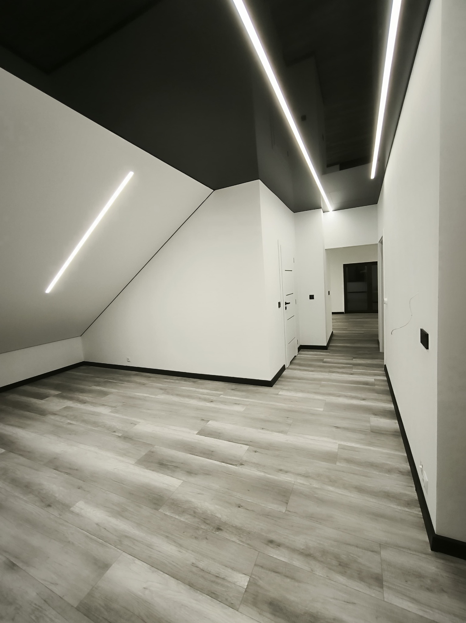 Nowoczesne wnętrze: białe ściany, szara podłoga imitująca drewno, czarny sufit z liniowym oświetleniem LED. Minimalistyczny design, widok na korytarz z drzwiami.