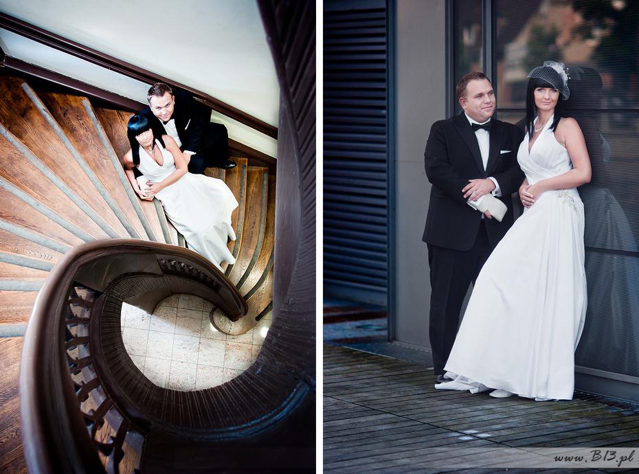 Para młoda: panna młoda w białej sukni z welonem i pan młody w czarnym smokingu, pozują na drewnianych kręconych schodach i na tle szklanej ściany z żaluzjami.