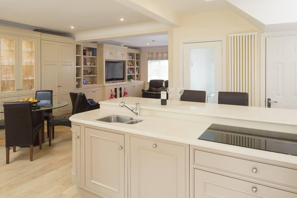 Jasna, elegancka kuchnia z wyspą i otwartym planem, widok na salon z zabudowaną biblioteczką i telewizorem, na blacie wyspy butelka wina i dwa kieliszki.