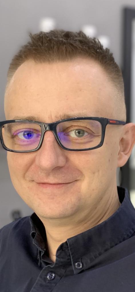 Portret mężczyzny w okularach z jednym okiem oświetlonym na niebiesko, uśmiechającego się do kamery w studio.