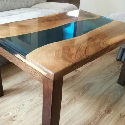 Stolik kawowy z blatem z drewna i żywicy epoksydowej w kolorze turkusowym, widoczne usłojenie drewna i refleksy światła na żywicy, na drewnianej podłodze.