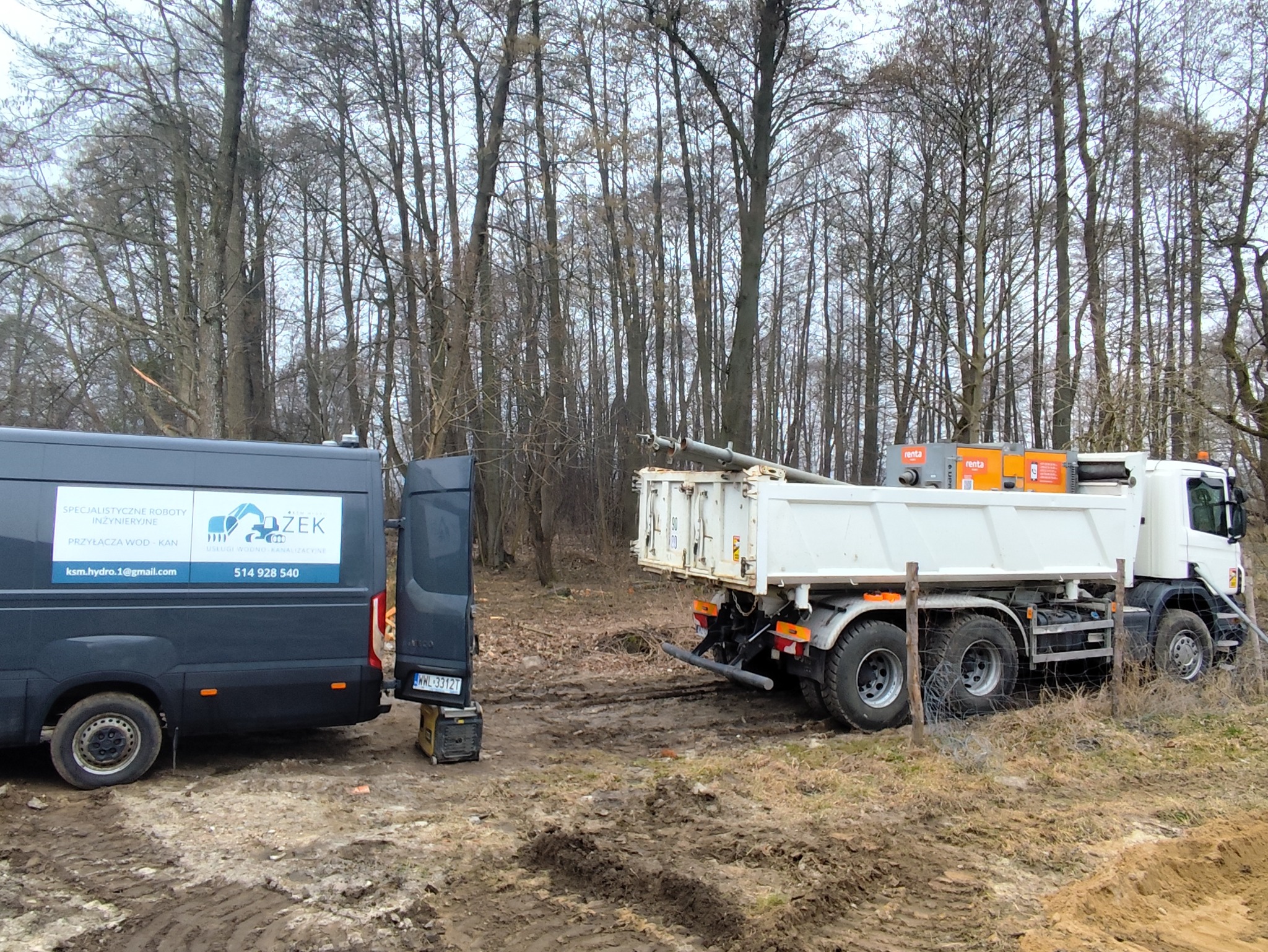 Ciężarówka i bus firmy inżynieryjnej na placu budowy, widoczne rury w skrzyni ładunkowej, logo firmy na busie z numerem telefonu i adresem email, teren błotnisty, w tle drzewa.