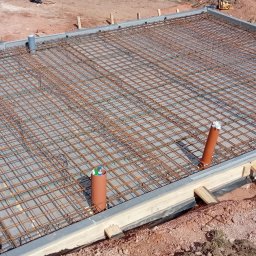 Grzegorz Kozicz - Zbrojenie płyty fundamentowej z rurami kanalizacyjnymi, widok z góry. Stalowa siatka na betonowej wylewce w szalunku, przygotowana do zalania betonem.