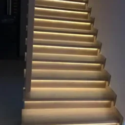 Drewniane schody z podświetleniem LED na każdym stopniu, widok z dołu, ciepłe światło