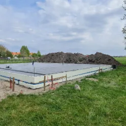 Przygotowany fundament pod budowę domu, z izolacją termiczną, widoczne prace ziemne i przygotowanie terenu.