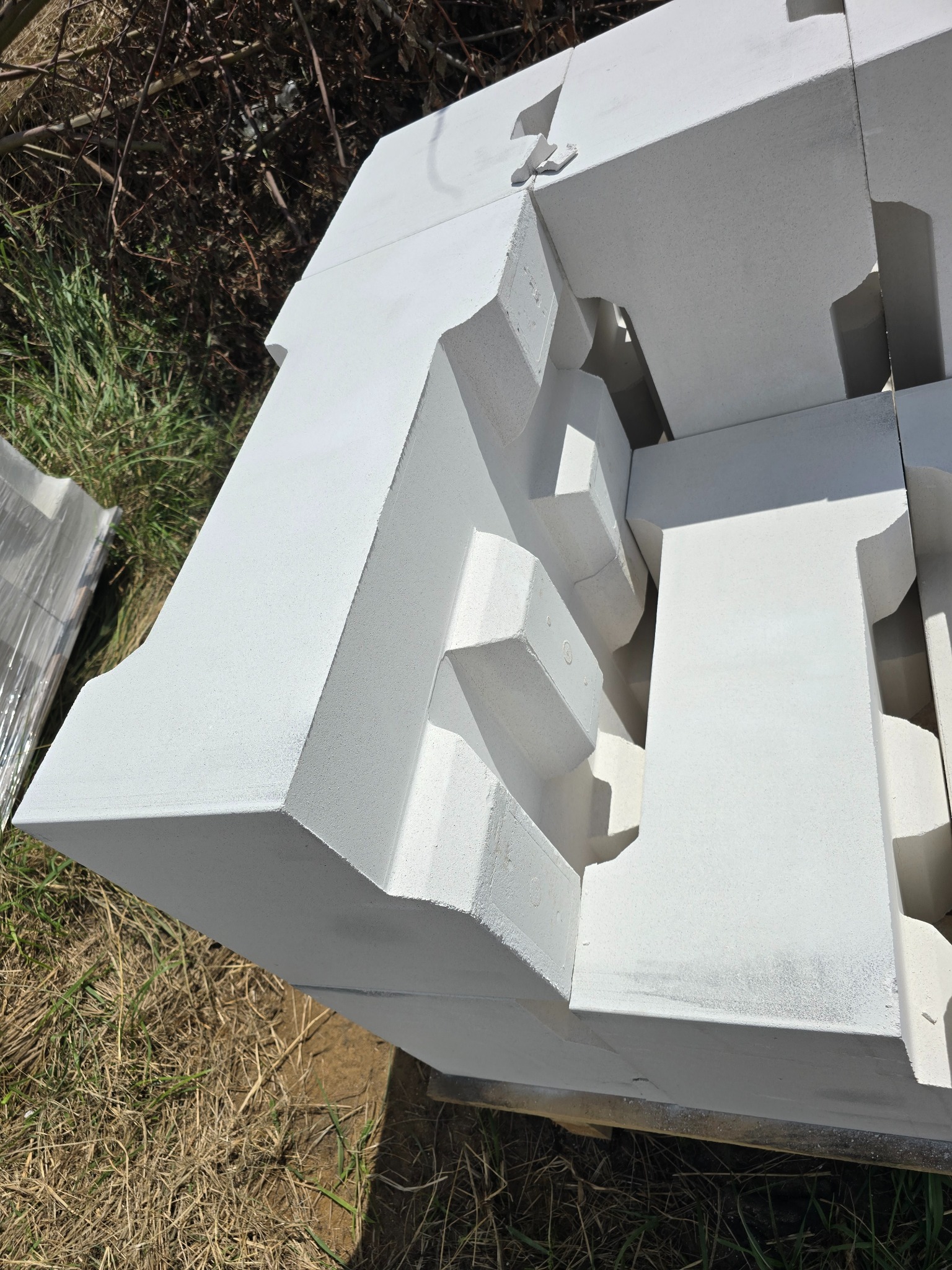 Białe bloczki fundamentowe z wyprofilowanymi krawędziami, składowane na trawie w Pisarzowicach, czekające na użycie.