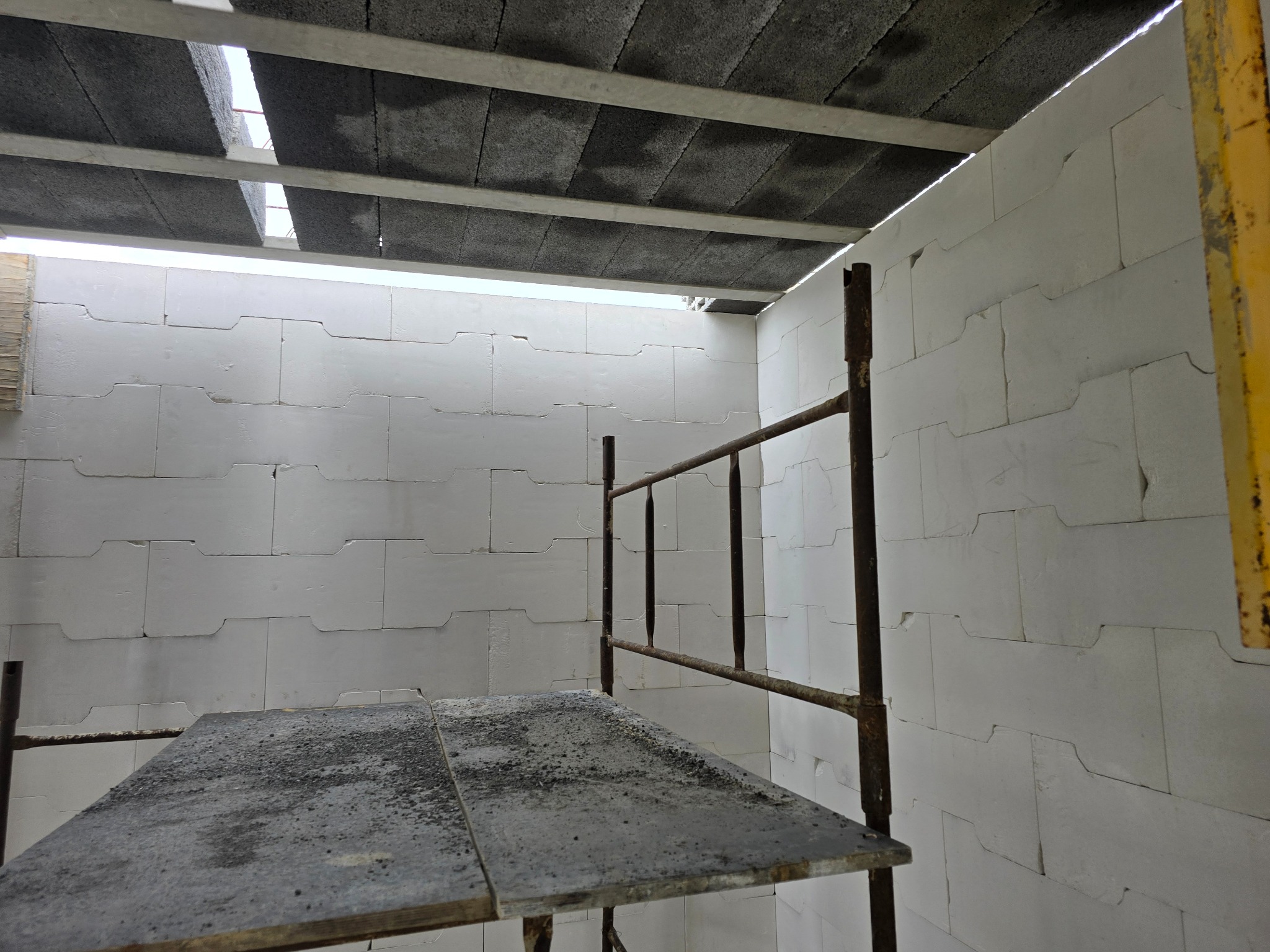 Wnętrze w trakcie budowy z białych bloczków, widoczne rusztowanie z metalowymi elementami i betonowy strop.