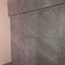 EMERWA Usługi wykończeniowe - Ściana wyłożona szarymi płytkami imitującymi marmur, z widocznym fragmentem sufitu i podłogi, w neutralnym oświetleniu.