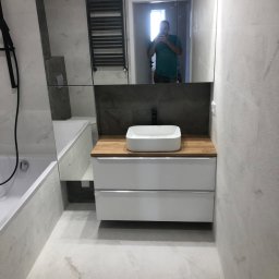 EMERWA Usługi wykończeniowe - Nowoczesna łazienka z umywalką nablatową na drewnianym blacie, szafką z szufladami, grzejnikiem drabinkowym i lustrem z odbiciem fotografa.