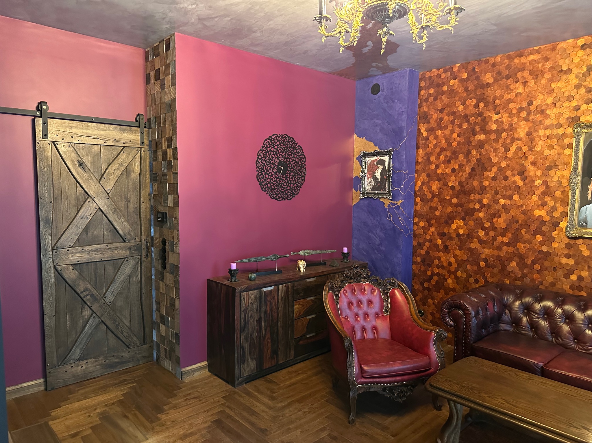 Salon z eklektycznym wystrojem: drewniane drzwi przesuwne w stylu rustykalnym, ściana w kolorze fuksji z dekoracyjną rozetą, komoda z ozdobami, krzesło i sofa w stylu vintage oraz ściana wyłożona...