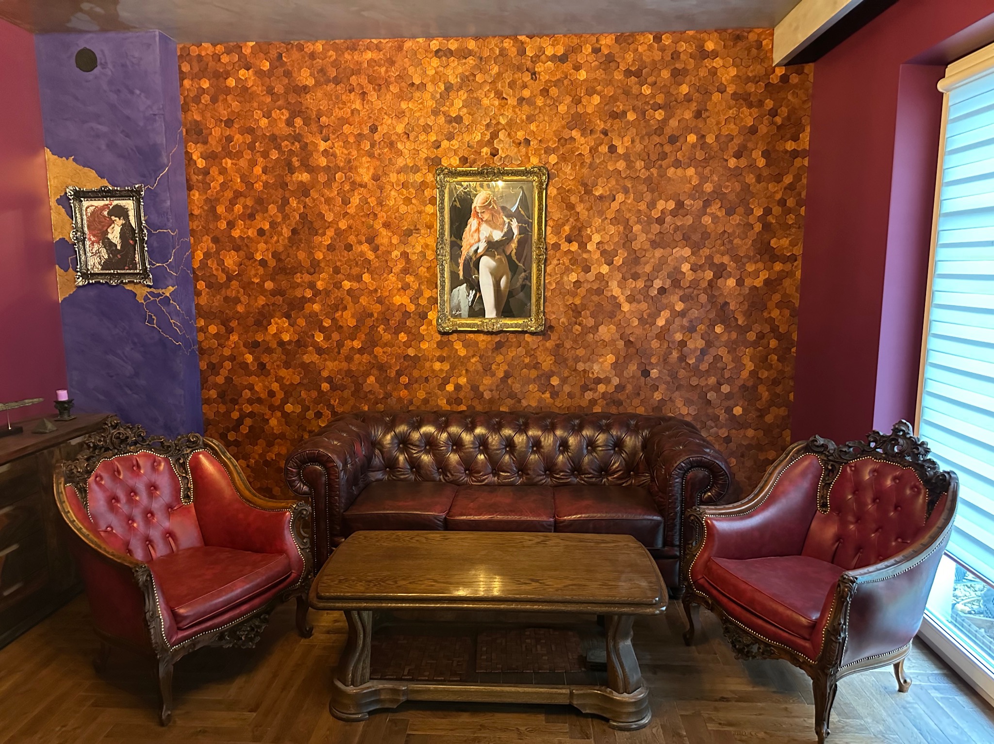 Elegancki salon w stylu vintage z brązową ścianą z heksagonów, skórzaną sofą Chesterfield, czerwonymi fotelami z rzeźbionymi ramami i drewnianym stolikiem kawowym.