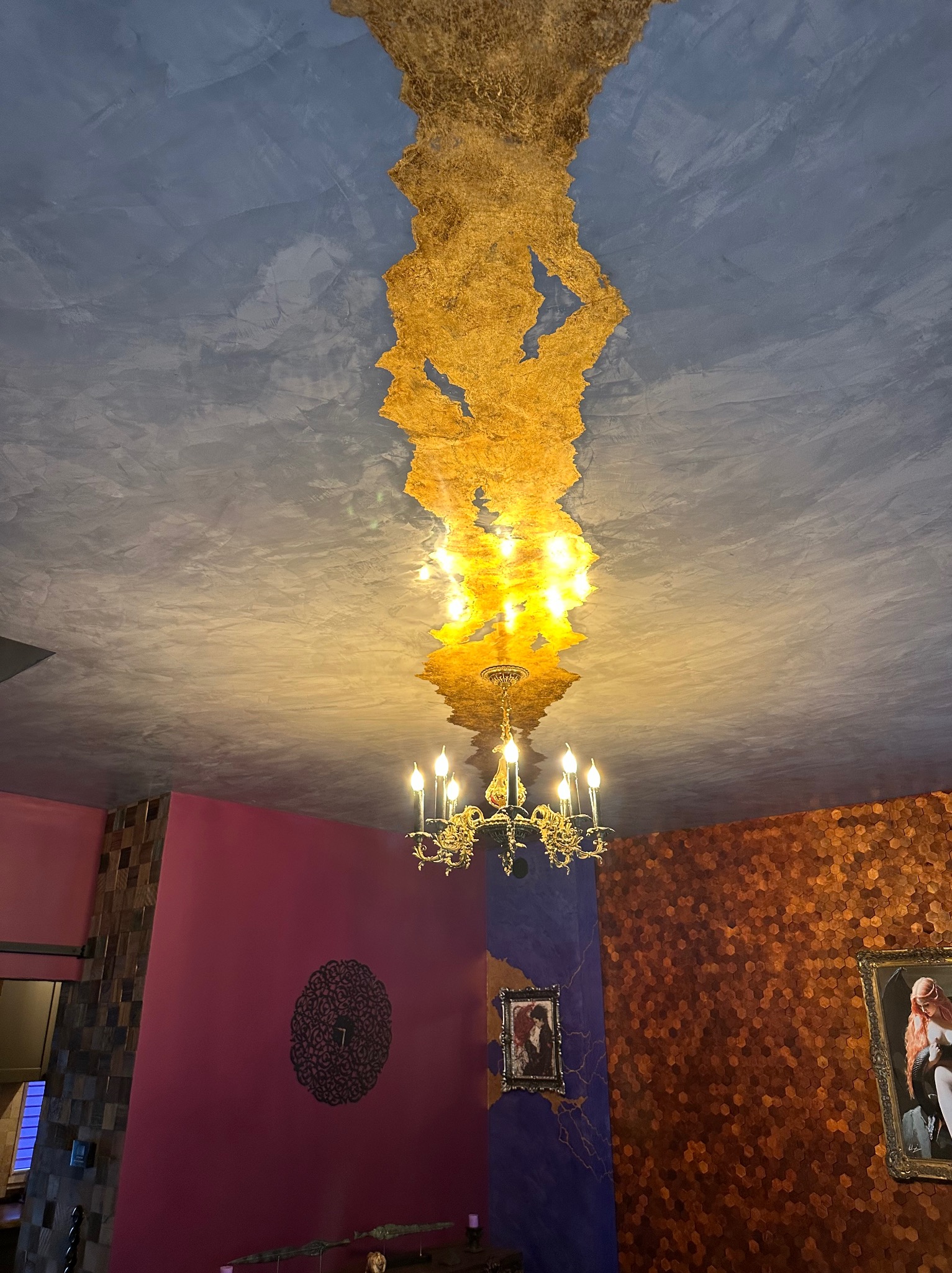 Ozdobny sufit z efektem złotej folii, centralnie umieszczony żyrandol z wieloma ramionami, ściany w odcieniach fuksji i miedzianych heksagonów, fragmenty dekoracji w stylu eklektycznym.