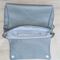 Otwarta, jasnoniebieska torebka z fakturą skóry, widoczna srebrna podszewka z zamkiem błyskawicznym i srebrny łańcuszek na boku.
