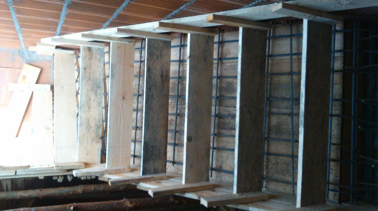 Deskowanie szalunkowe zbrojenia pionowego, przygotowane do zalania betonem, widoczne drewniane podpory i siatka z prętów stalowych.