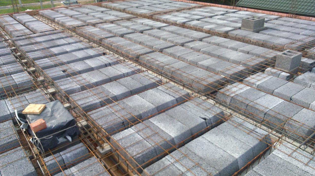 Szary strop Teriva z żebrami i pustakami betonowymi, widoczne zbrojenie z drutu, fragment dachu w tle.